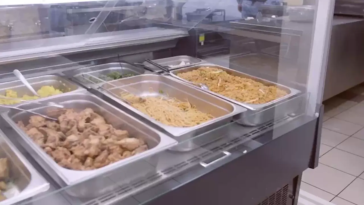 Warmhoudbakken met bami en gebakken kip achter de toonbank.